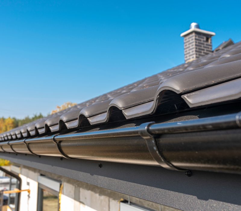 A metal, black gutter on a roof covered with ceramic tiles. Close up shot.